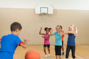 Diverse elementary students playing basketball in gym class