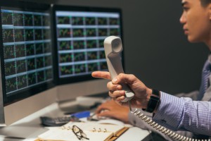 Hand of financial broker holding telephone receiver and pointing at the computer screen