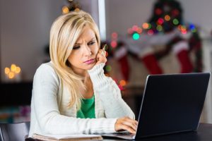 Woman concerned while looking at bank account on laptop at Christmastime